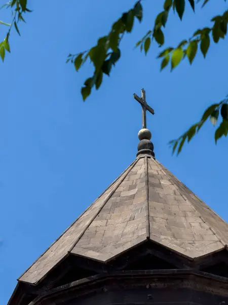 Binanın tepesinde bir haç var. Bina ağaçlarla çevrili. Gökyüzü mavi