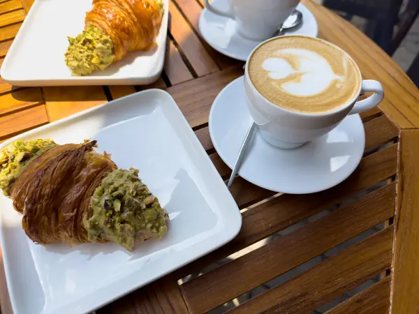 Tahta bir masanın üzerinde bir tabak kruvasanla birlikte beyaz kahve bardağı kapuçino. Kafede kahvaltı, Paris sabahı, Avrupa sabahı. Yüksek kalite fotoğraf