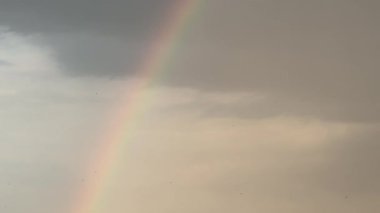 Bir şehrin üzerinde gökkuşağı görülür. Gökkuşağı uzun ve gökyüzü boyunca uzanıyor.