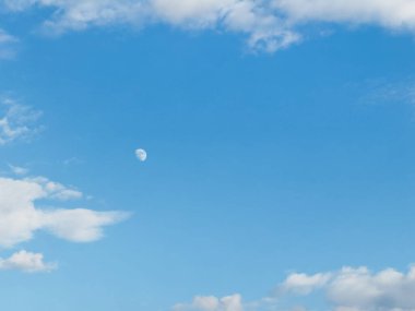 Ay gökyüzünde ışıl ışıl parlıyor, mavi alana gümüş bir parıltı saçıyor. Gökyüzünün ortasında, tüylü beyaz bulutlarla çevrili. Gökyüzü berrak ve lekesiz