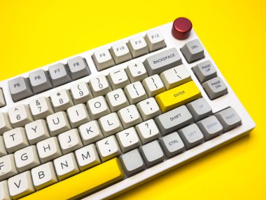 Parlak sarı arka planda Enter tuşuna sahip beyaz mekanik klavye, minimalizm, klavye tuşları. Sol altta sarı tuş olan bir klavye. Klavyede büyük harf kilit tuşu ve kaydırma tuşu var.