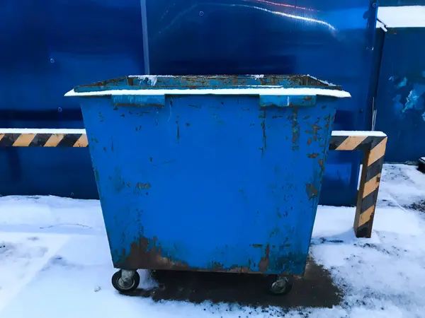 Üzerinde sarı çizgili mavi bir çöp konteynırı. Karlı bir yere park edilmiş.
