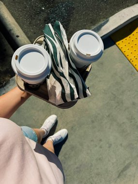 Kapuçino ve seyahat. Bir kişi iki fincan kahve ve bir peçete tutuyor. Bardaklar beyaz ve kapakları var.