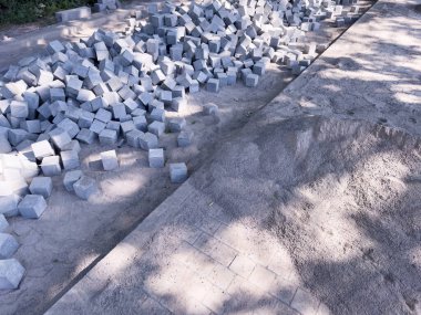 İnşaat alanı, kırık patika, yol onarımı, beton. Yerde bir kaldırımın yanında gri tuğla yığını var. Tuğlalar dağılmış ve bazıları yığılmış.