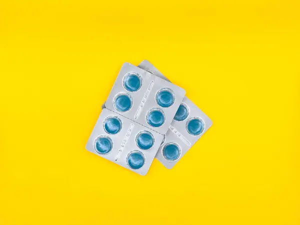 Beyaz arka planda mavi bir hap duruyor. Hap kare şeklinde ve mavi bir merkezi var. Boşluğu kopyala, kabuğu soy, üst görünümü kaydet