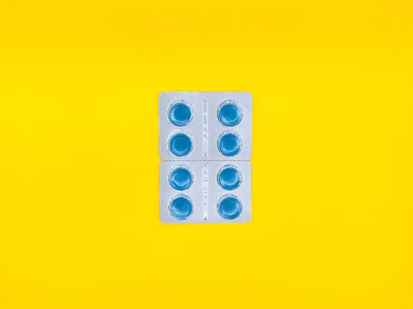 Beyaz arka planda mavi bir hap duruyor. Hap kare şeklinde ve mavi bir merkezi var. Boşluğu kopyala, kabuğu soy, üst görünümü kaydet