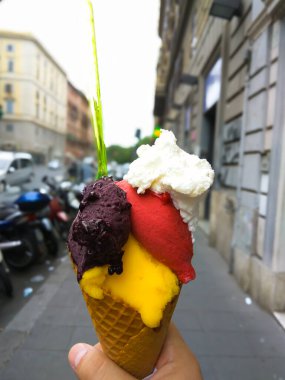 Kahverengi, pembe ve turuncu kıvrımlı dondurma külahı tutan biri. Yüksek kalite