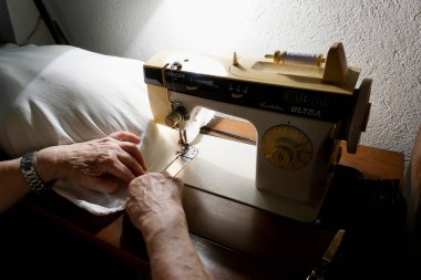 Yaşlı bir kadın dikiş makinesine yastık dikiyor. Yaşam tarzı, hobiler, el sanatları ve ev projeleri için mükemmel..