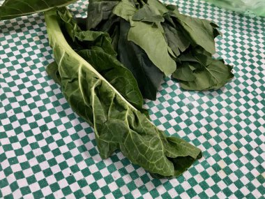 Yeşil bir masa örtüsü üzerinde çiğ pazı, kırsal bir mutfak ortamında yemek pişirmeye hazırlanıyor..