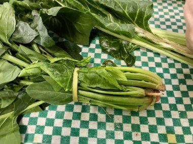 Yeşil bir masa örtüsü üzerinde çiğ pazı, kırsal bir mutfak ortamında yemek pişirmeye hazırlanıyor..