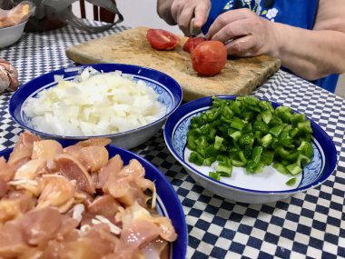 Kareli bir masa örtüsünde, içinde doğranmış tavuk, domates, biber, soğan ve sarımsak bulunan malzemeler pişiriyorum..