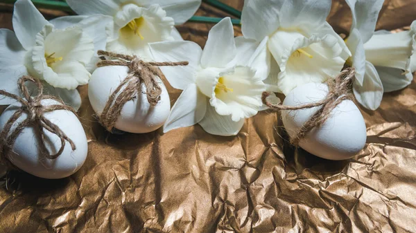 White Easter eggs with flowers on golden background, close up. Concept of Easter Sunday,  religious traditions and symbolism