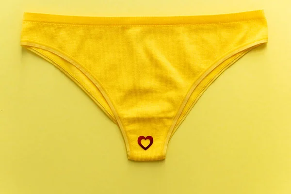 stock image Top view of colorful females panties with red heart confetti on  yellow background, close up. Cotton underpants. Concept of woman health care, menstruation and feminine hygiene