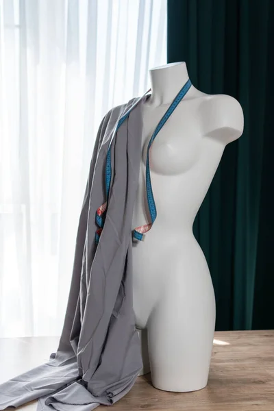 White modern mannequin or dressmakers dummy with gray fabric and hanging measuring tape, closeup. Concept of sewing workshop
