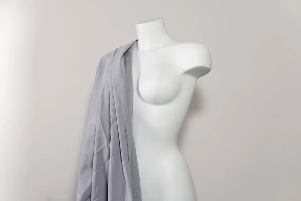 White mannequin or dressmakers dummy with gray fabric on light background, close-up. Concept of sewing workshop