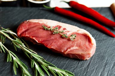 Raw organic beef meat with rosemary, seasonings, salt and red pepper  on black background, close-up. Preparing to cooking steak