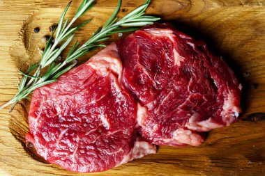 Raw organic beef meat with rosemary, seasonings, salt and red pepper  on wooden cutting board, close-up. Preparing to cooking steak