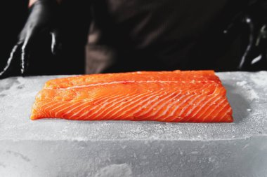 Close-up of chef hand prepared to cooking fresh salmon fillet, black background. Raw fish on the block of ice