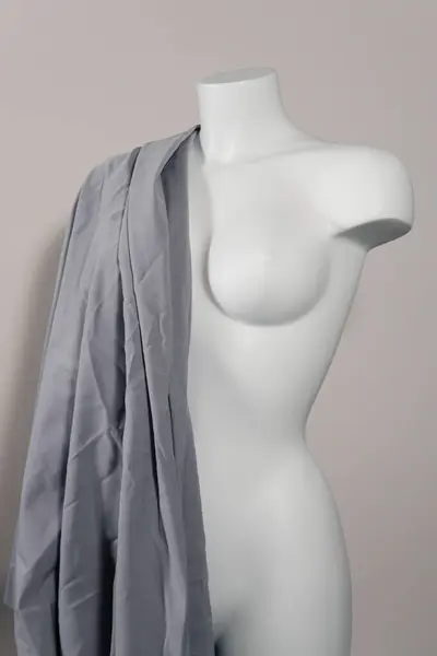 White modern mannequin or dressmakers dummy with gray fabric and hanging measuring tape, closeup. Concept of sewing workshop