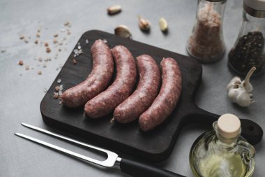 Kesme tahtasının üstünde ızgara sosis ızgara çatal, tuz ve biber, gri arka plan, kapat. Sağlıksız yiyecekler. Pişirme hazırlığı