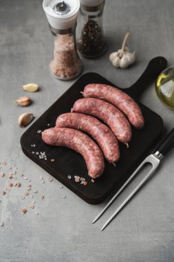 Kesme tahtasının üstünde ızgara sosis ızgara çatal, tuz ve biber, gri arka plan, kapat. Sağlıksız yiyecekler. Pişirme hazırlığı