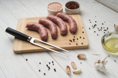 Ahşap kesme tahtasının üzerinde ızgara sosis ızgara çatal, tuz ve biber, beyaz arka plan, kapat. Sağlıksız yiyecekler. Pişirme hazırlığı