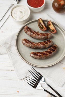 Tabakta ızgara sosis yemeye hazır, beyaz ahşap arka plan, kapat. Sağlıksız yemek.
