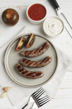 Tabakta ızgara sosis yemeye hazır, beyaz ahşap arka plan, kapat. Sağlıksız yemek.