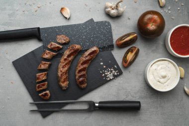 Kesme tahtasında ızgara çatal ve bıçakla ızgara sosis yemeye hazır. Gri arka plan, kapat. Sağlıksız yemek.