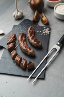 Kesme tahtasında ızgara çatal ve bıçakla ızgara sosis yemeye hazır. Gri arka plan, kapat. Sağlıksız yemek.