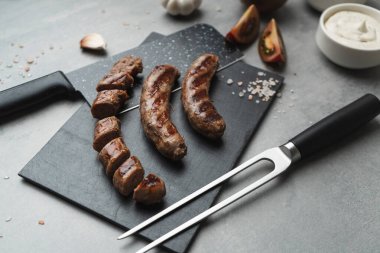 Kesme tahtasında ızgara çatal ve bıçakla ızgara sosis yemeye hazır. Gri arka plan, kapat. Sağlıksız yemek.