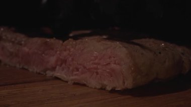 Erkek aşçı elleri ahşap kesme tahtasındaki bıçakla biftek doğruyor, yakın çekim. Ağır çekim. Gıda hazırlama süreci ve restoran hizmeti kavramları.