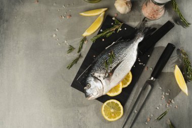 Limonlu taze dorado balığı, biberiye ve siyah kesme tahtasındaki baharatlar, yakın çekim. Gri masadaki malzemeli çiğ deniz ürünleri. Sağlıklı gıda konsepti