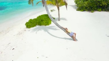 Beautiful woman lies on a palm tree on a white sand beach and turquoise sea on tropical island. Aerial drone view