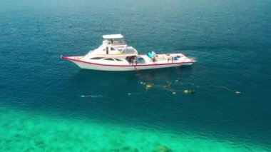 Fishermen on a white boat take out fishing nets with caught fish near a local island in the Maldives. Aerial drone view turquoise sea