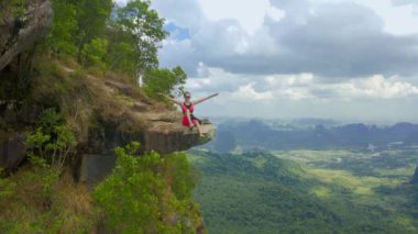 Genç bir kadın bulut gününde uçurumun kenarında oturur. Ejderha Tepesi - Khao Ngon Nak Krabi ili, Tayland