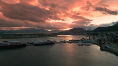Gün batımında Ushuaia limanının havadan görünüşü, arkasında dramatik gökyüzü ve dağlar var.
