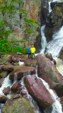 Kazakistan 'da yemyeşil bir şelale ve kayalık arazide manzaranın tadını çıkaran ziyaretçilerin olduğu bir kanyon..