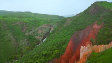 Kazakistan 'daki kırmızı kanyonun çarpıcı manzarası yemyeşil ve çağlayan bir şelale arasında canlı kırmızı kaya oluşumları sergiliyor.