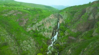 Sersemletici bir şelale, Kazakistan 'daki yemyeşil yemyeşil kayalıkların arasında kayalık bir uçurumdan aşağı yuvarlanıyor. Etrafı sakin dağlık araziyle çevrili.