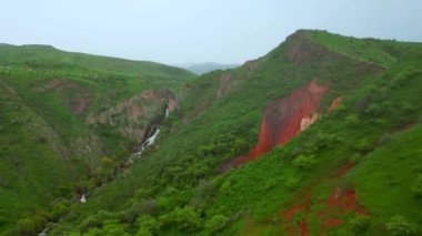 Kazakistan 'daki canlı kırmızı kanyonda yemyeşil ve çağlayan şelalelerle çelişen jeolojik oluşumlar sergileniyor.