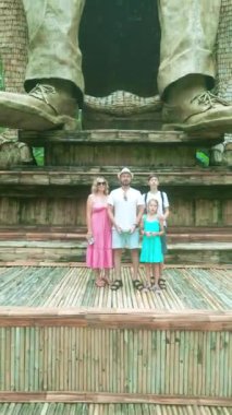 Neşeli bir aile, Tegalalang, Ubud 'un yemyeşil pirinç teraslarının ortasında büyük bir heykelin önünde poz veriyor..