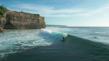 Balangan, Bali 'nin baş döndürücü kayalıklarında sörf yapan bir sörfçünün hava görüntüsü..