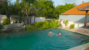 İki çocuk yemyeşil ve geleneksel Bali mimarisi ile çevrili sakin bir havuzda yüzmeyi seviyor..