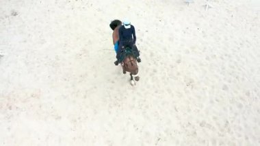 Kumlu binicilik sahasında bir engelin üzerinden atlamaya hazırlanan bir binicinin hava görüntüsü.