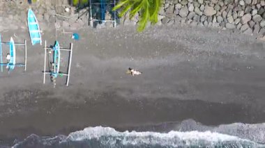 Sulawesi, Endonezya 'daki çakıl taşlı bir plajda, etraflarında palmiye yapraklarıyla rahatlayan iki insanın hava görüntüsü..