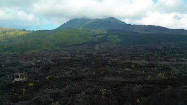 Bali 'de siyah lav akıntıları ve dağınık yeşillik içeren engebeli Batur Dağı manzarası..