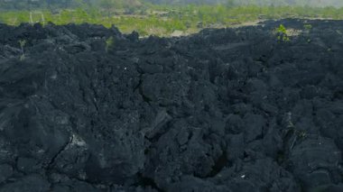 Katılaşmış siyah lav manzarasının havadan görünüşü, yeşillik ve uzak bir yapı ile karışmış engebeli araziyi gösteriyor..