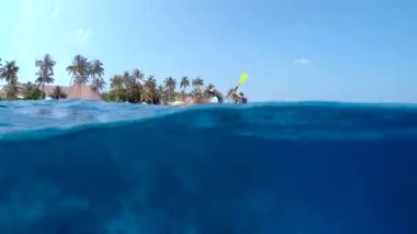 İki kano, verimli palmiye ağaçları ve canlı tropikal manzarayla çevrili Maldivler 'in berrak sularında süzülüyor..