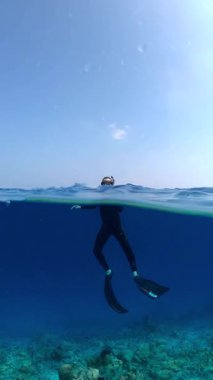 Şnorkelli bir insan Maldivler 'de okyanus yüzeyinin hemen altında yüzüyor. Arka planda mercanlar görünüyor..